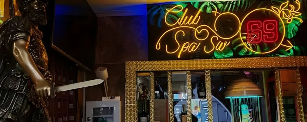 Entrada de Club SW69 en Bogotá con el aviso de neón «Club Spa Sw 69» sobre follaje tropical iluminado