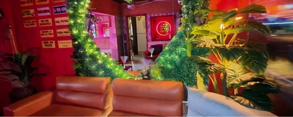 Zona social de Club SW69: sofás de cuero, muros de follaje artificial con luces y un neón circular al fondo