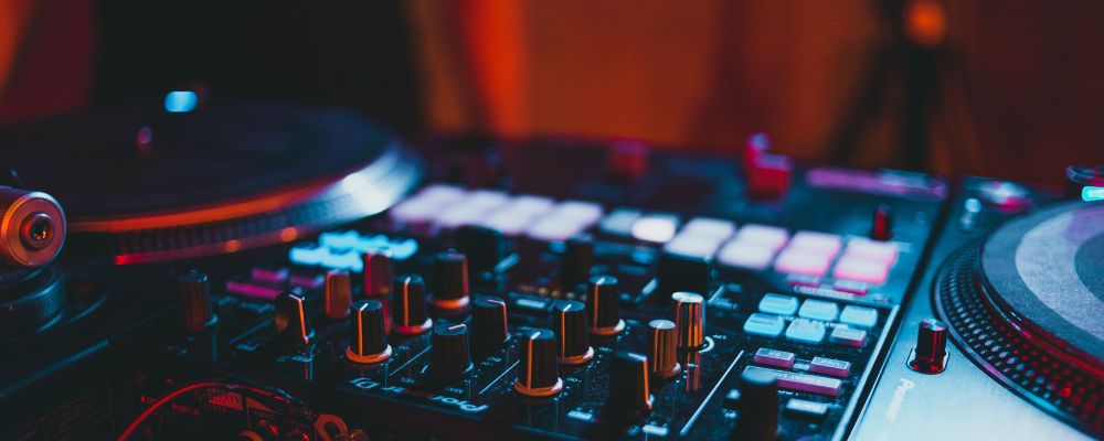Consola de DJ con tornamesas iluminada en tonos azules y rojos, ilustración del componente de discoteca de los clubes de Cali
