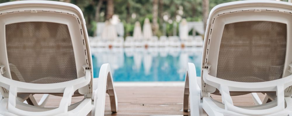 Camastros blancos frente a una piscina rodeada de palmeras, ambiente de clima cálido como el de Cali