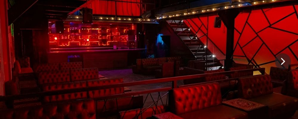 Zona de Rumba de Imperio SW en Bogotá: sofás chesterfield rojos, barra con luces de neón y escalera al fondo