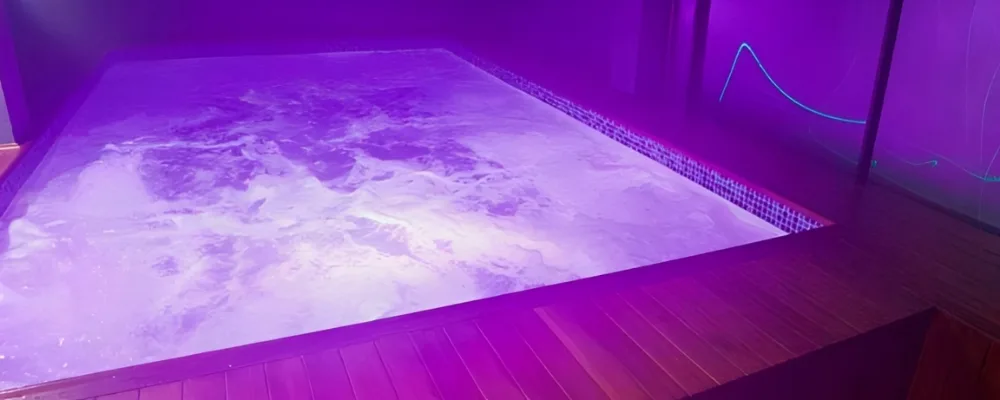 Jacuzzi de Insolitam Spa Bar Swinger Bogotá, con agua en movimiento e iluminación violeta sobre deck de madera