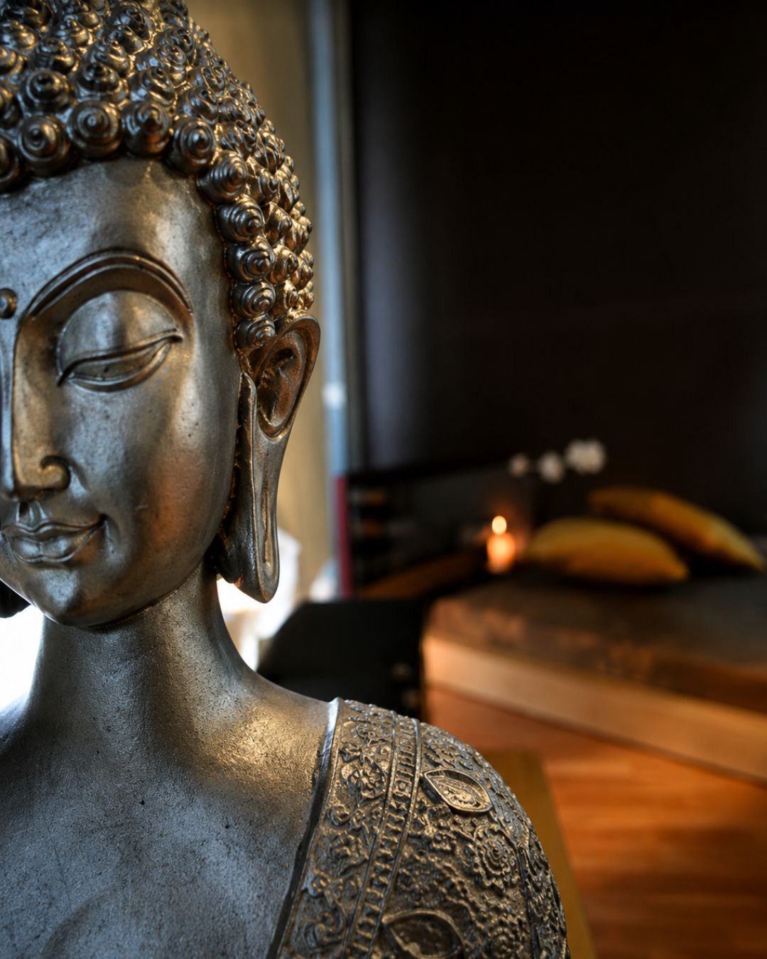 Figura de Buda en bronce en primer plano y camilla con velas al fondo, en Zoe Thai Spa